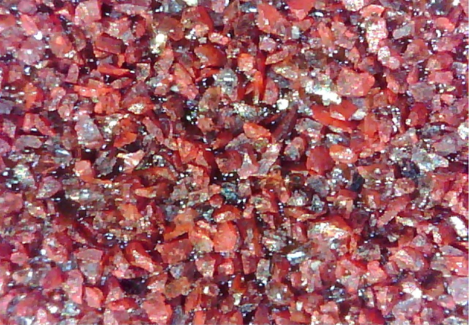 Close-up of red aluminum oxide abrasive grit particles used in sanding belts for wood sanding. 